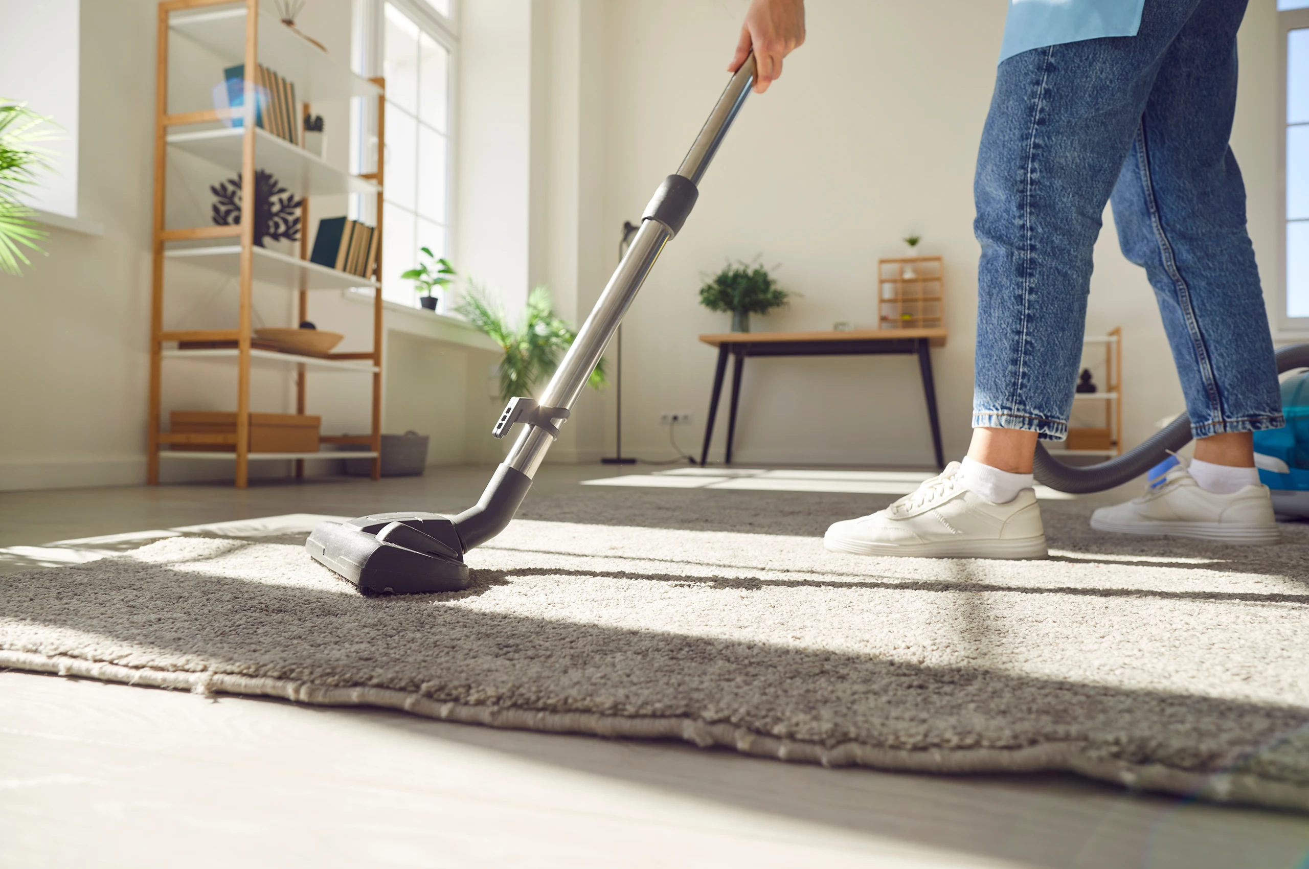 Person saugt Teppich in hellem Wohnzimmer mit Sonnenlicht