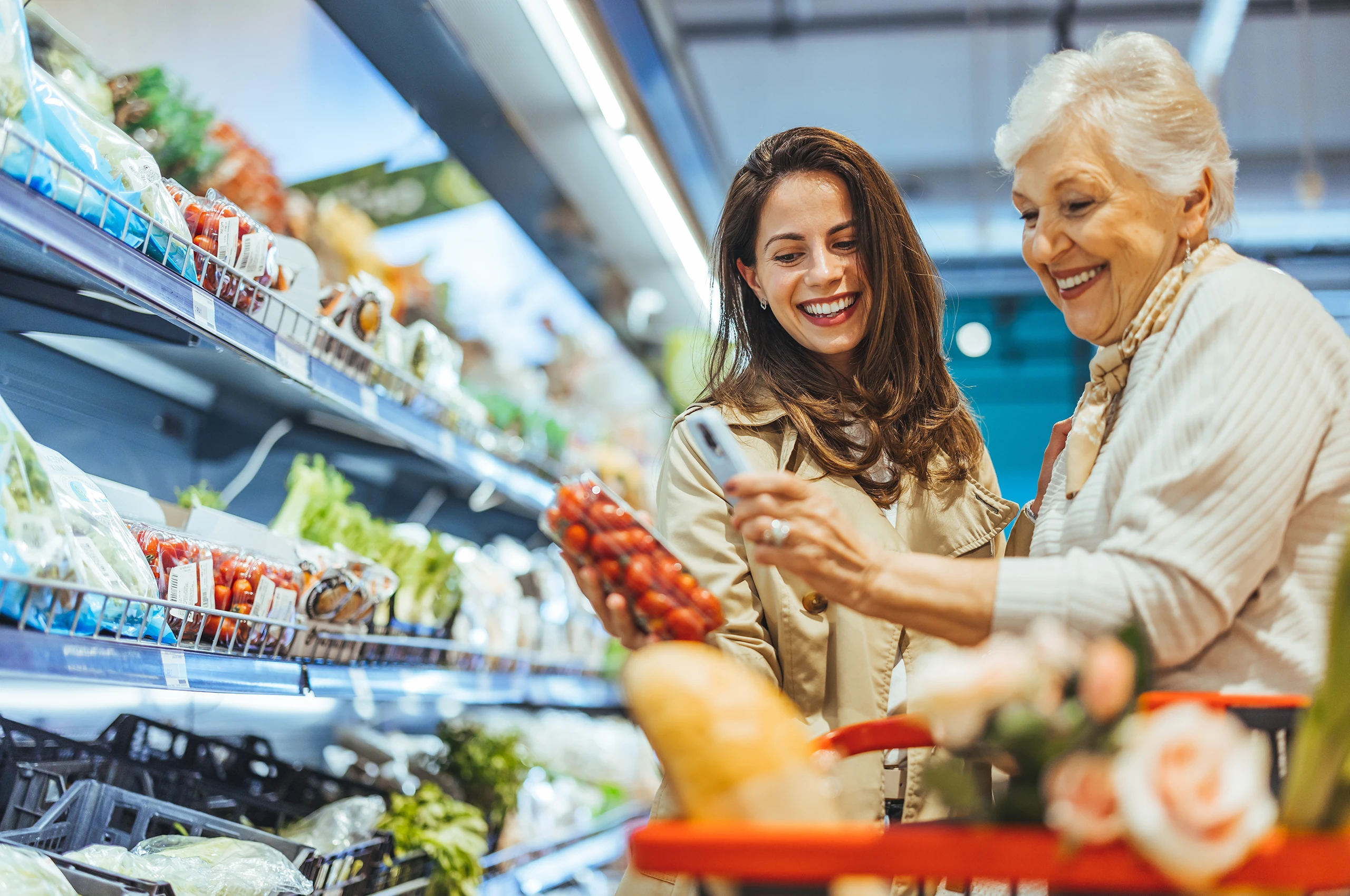 Junge Frau und ältere Dame kaufen gemeinsam frisches Obst und Gemüse im Supermarkt.