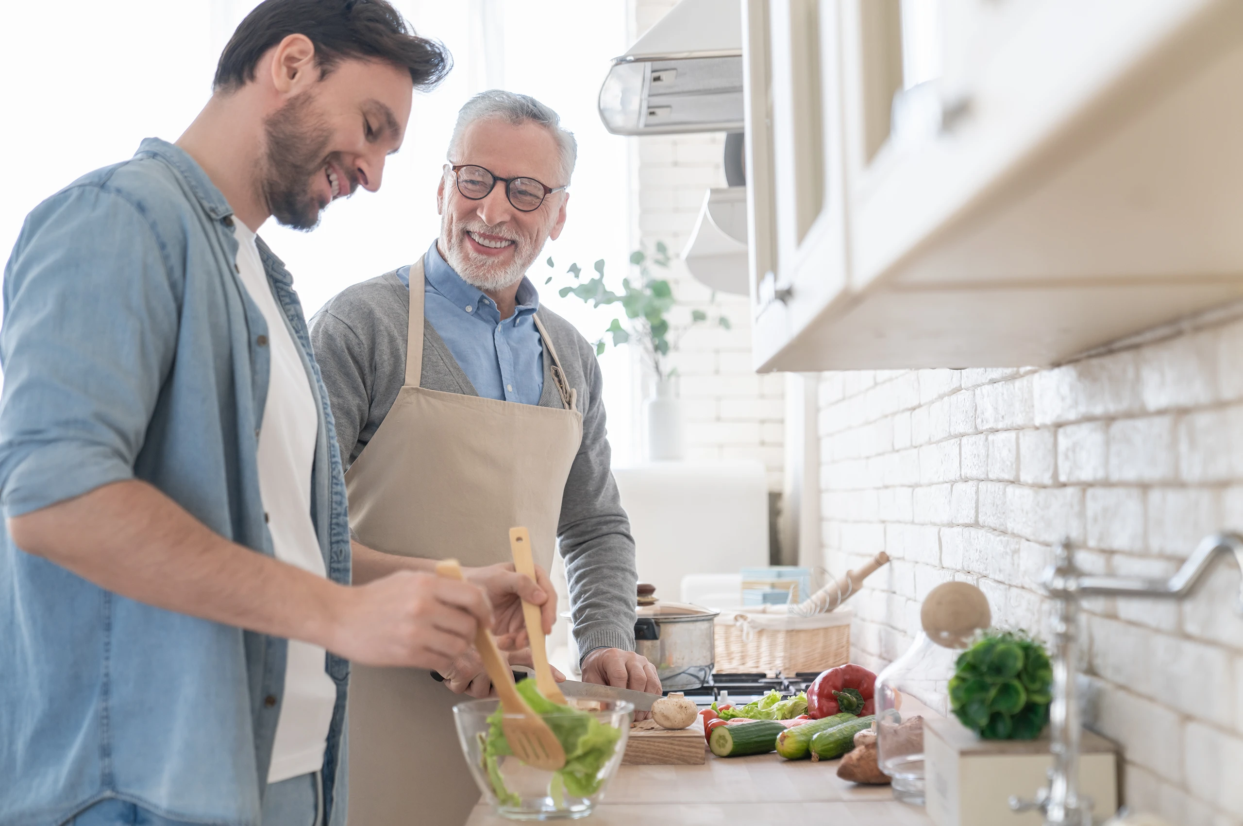 Junger Mann und Senior kochen gemeinsam und lachen dabei